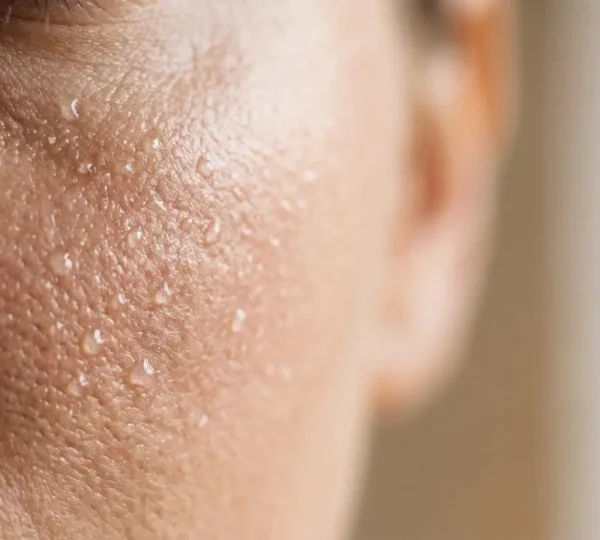 Gros plan photographique d'une peau hydratée reflétant naturellement la lumière, avec des textures de gouttes d'eau sur une surface cutanée